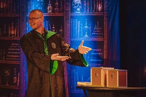 Iluzjonista prezentuje magiczne skrzynie w scenografii inspirowanej szkołą magii
