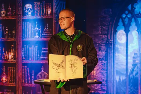 Iluzjonista prezentuje dzieciom księgę magicznych stworzeń podczas pokazu iluzji