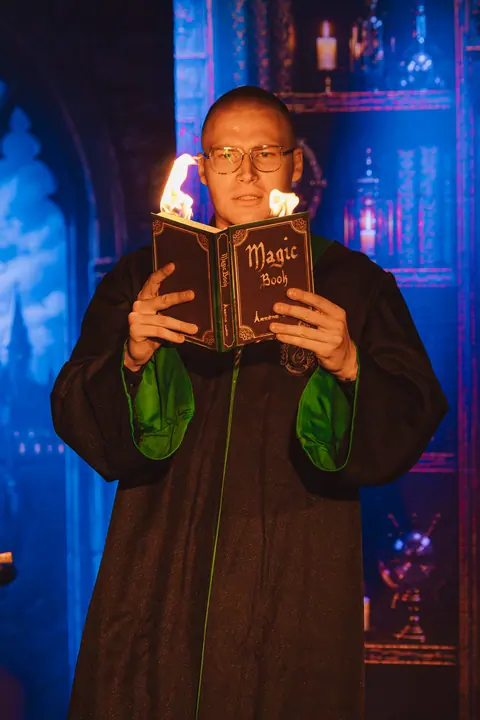 Pokaz magii dla dzieci — iluzjonista trzyma płonącą magiczną księgę zaklęć